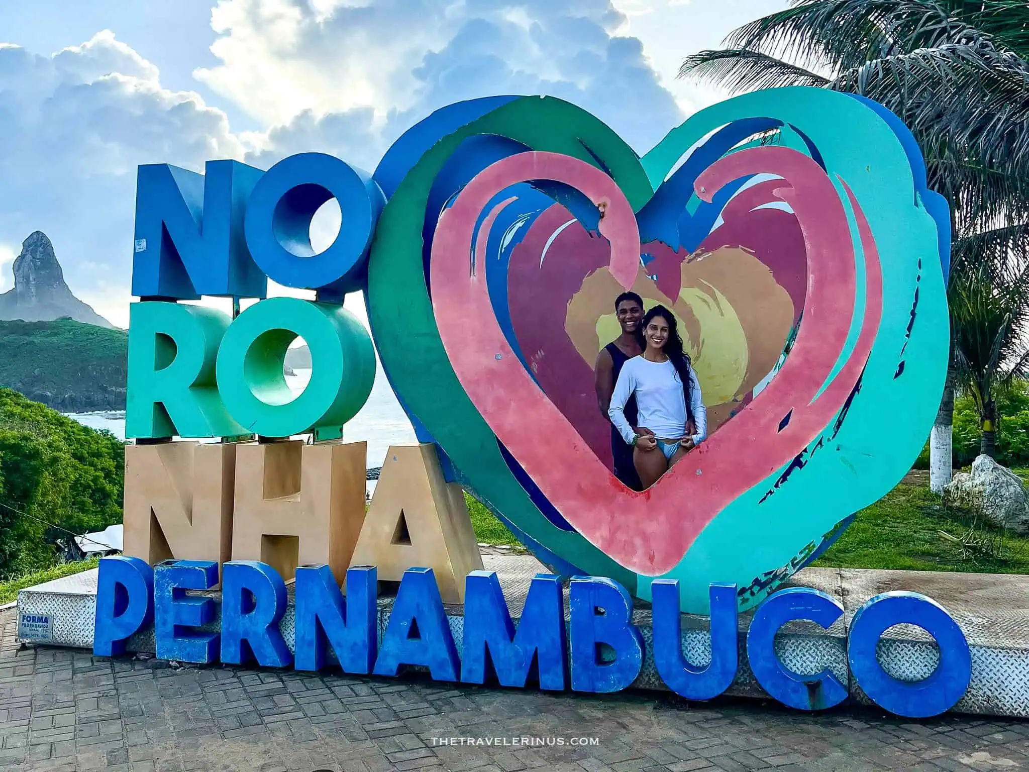 thais and kelvyn posing with noronha pernambuco sign with morro do pico in the background, Fernando de Noronha