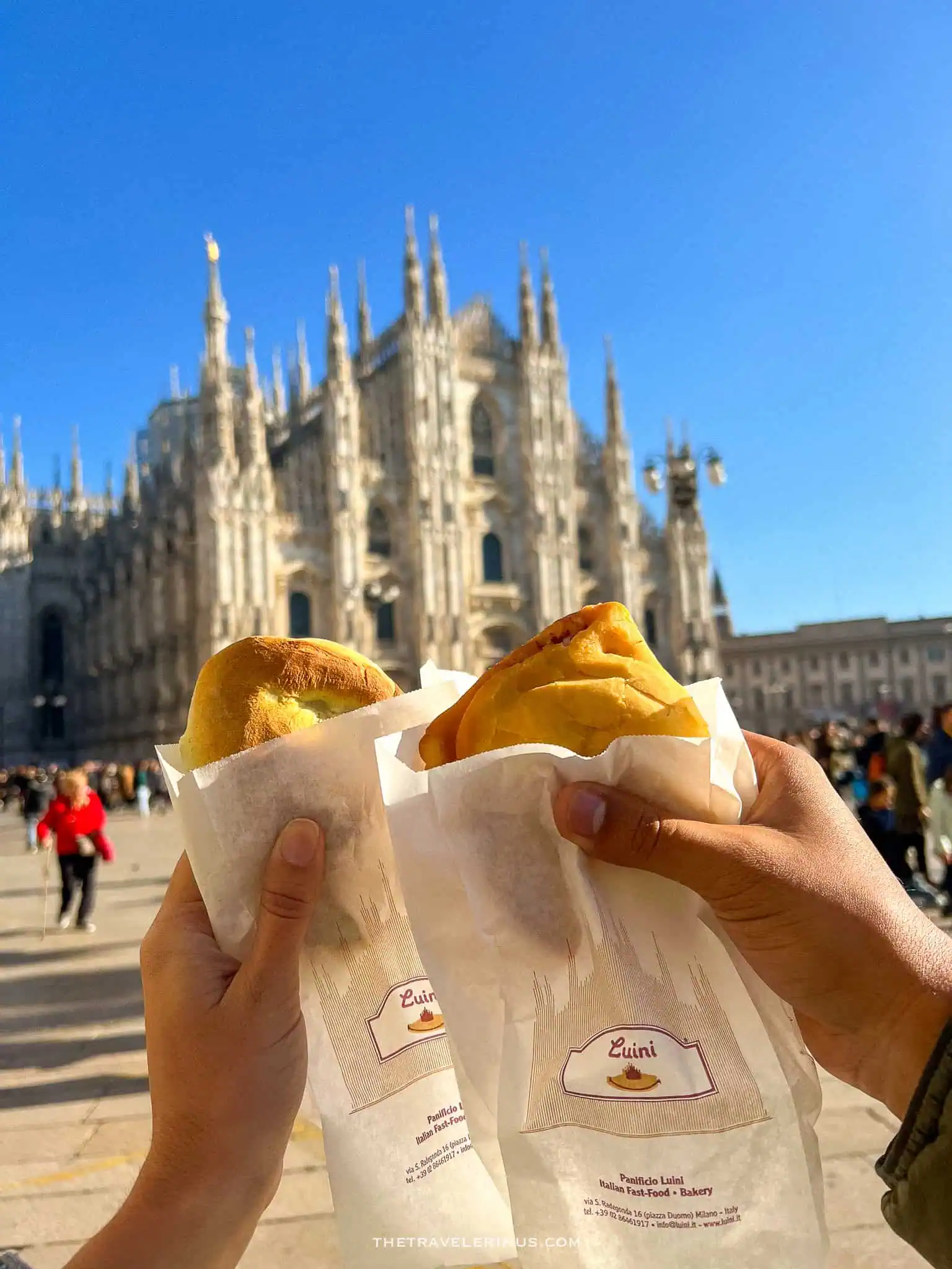 holding 2 Panzerotti with the Milan cathedral in the background